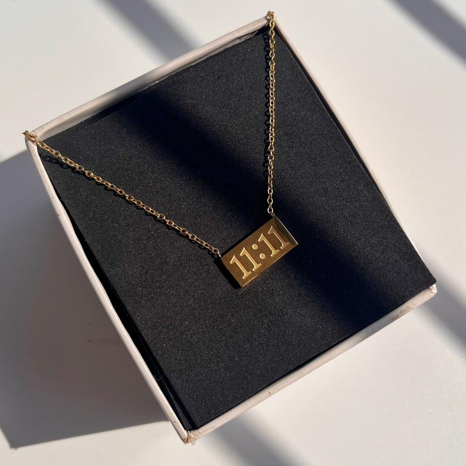 Gold necklace with a rectangular tag on a black box