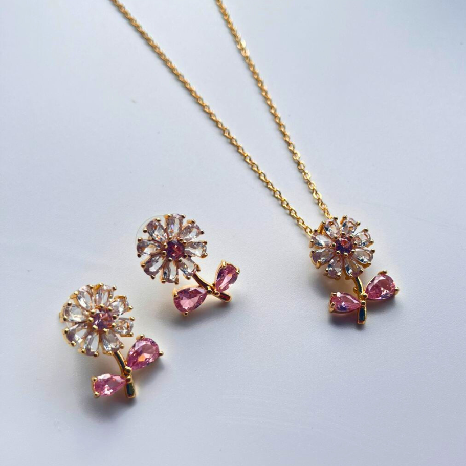 Gold necklace and earrings with pink gemstones on a light gray background