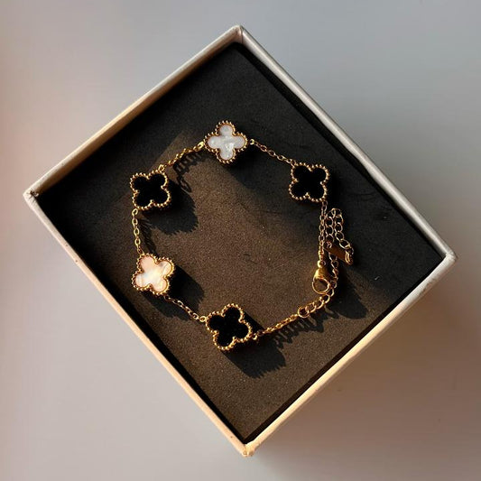 Gold bracelet with clover charms in a box on a soft gray background