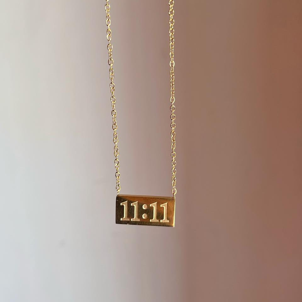 Gold necklace with '11:11' pendant on a gradient background