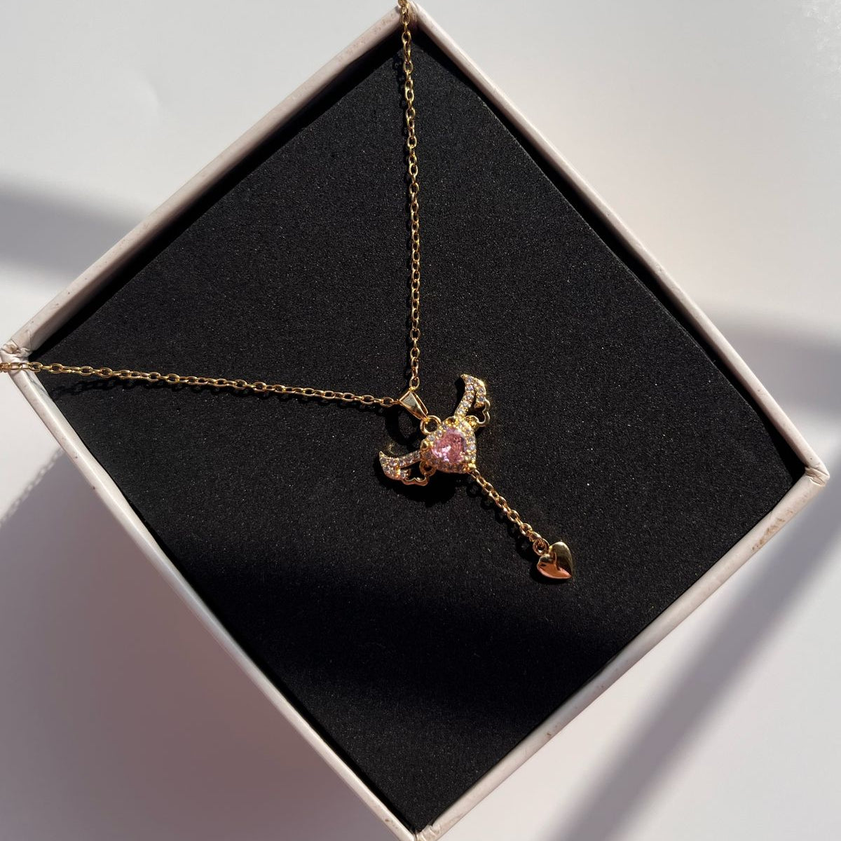 Gold necklace with a pink gemstone pendant in an open box on a light gray background