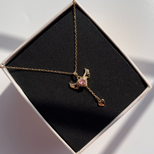 Gold necklace with a pink gemstone pendant in an open box on a light gray background
