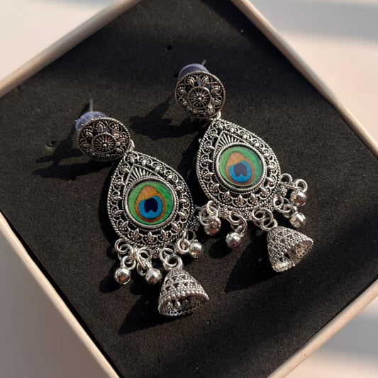 Ornate silver earrings with green and blue gemstones on a black box.