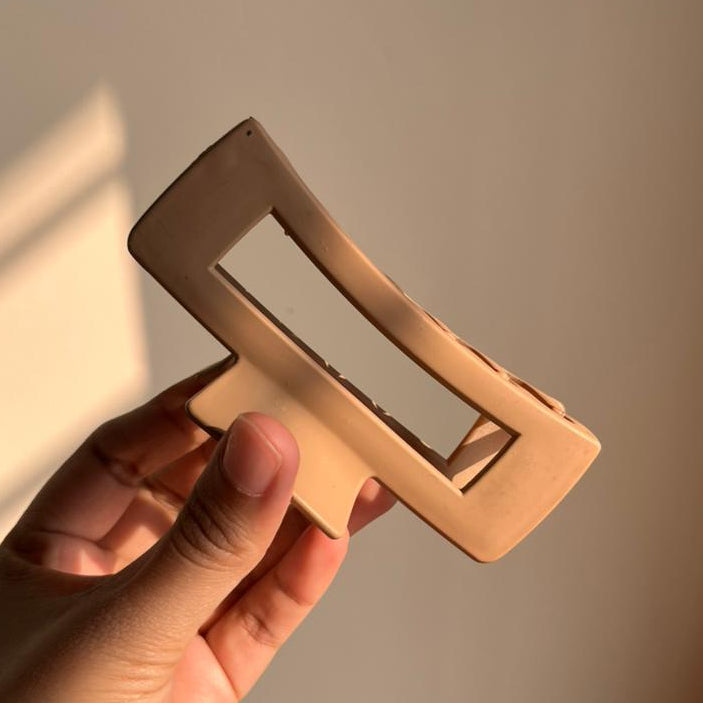 Hand holding a rose gold rectangular hair clip against a neutral background