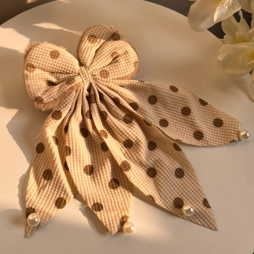 Polka dot bow hair clip on a white surface with flowers in the background