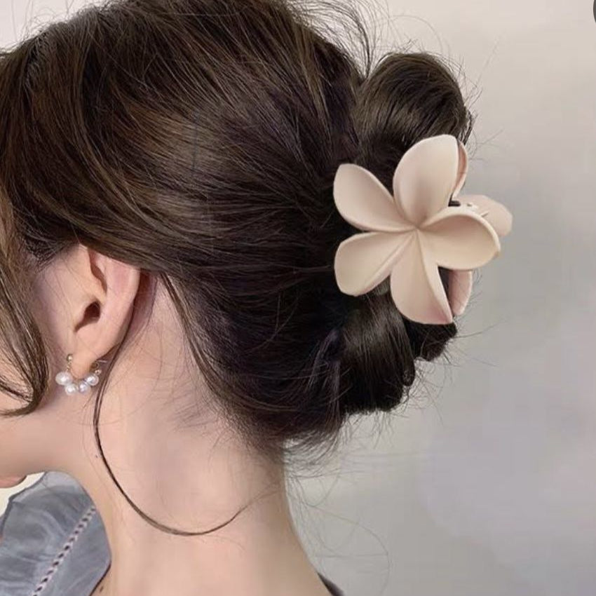 Woman with a stylish hair bun adorned with a beige flower accessory against a neutral background