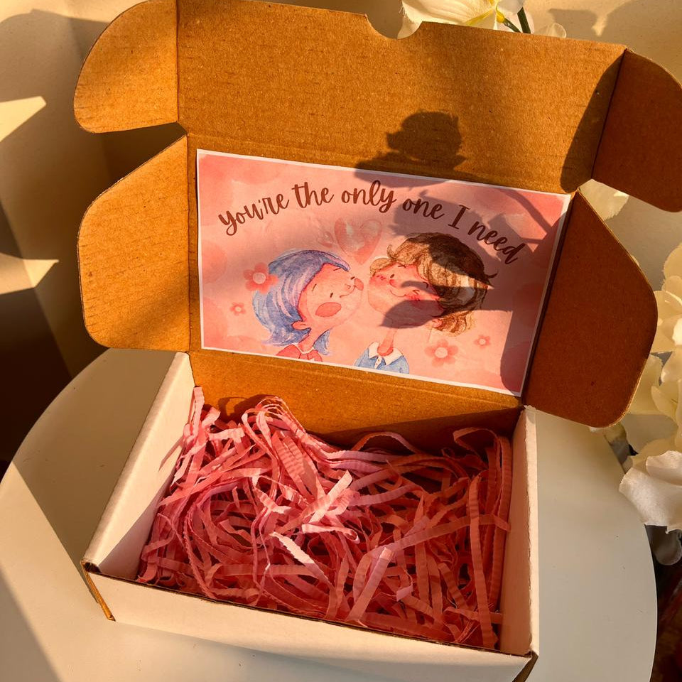 Open box with pink ribbon and a card inside, set against a soft background.