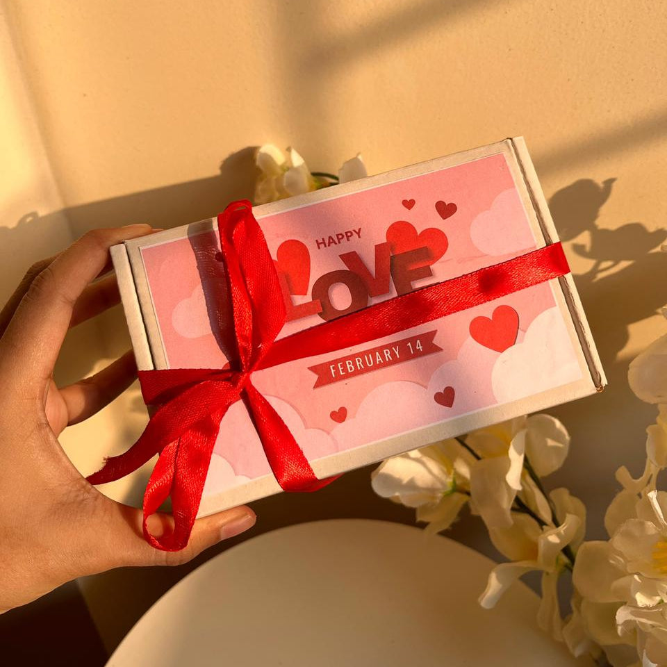 Gift box with 'Happy Love February 14' text and red ribbon held by a hand against a light background.