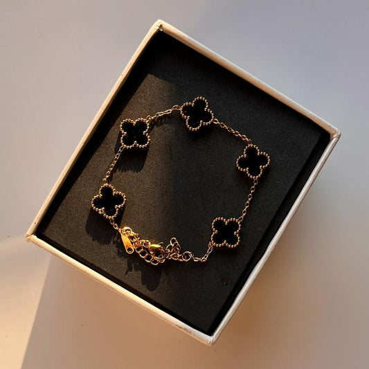 Gold bracelet with clover designs in a box on a light background