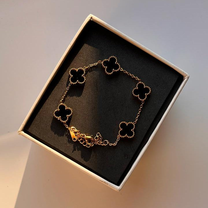 Gold bracelet with clover designs in a box on a light background
