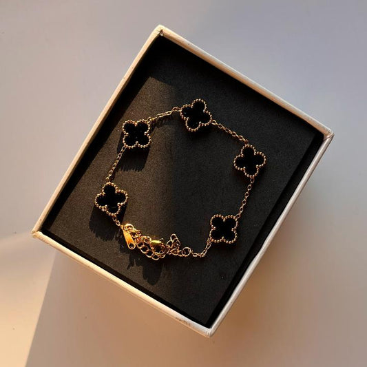 Gold bracelet with clover designs in a box on a light background