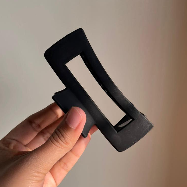 Hand holding a black hair clip against a neutral background