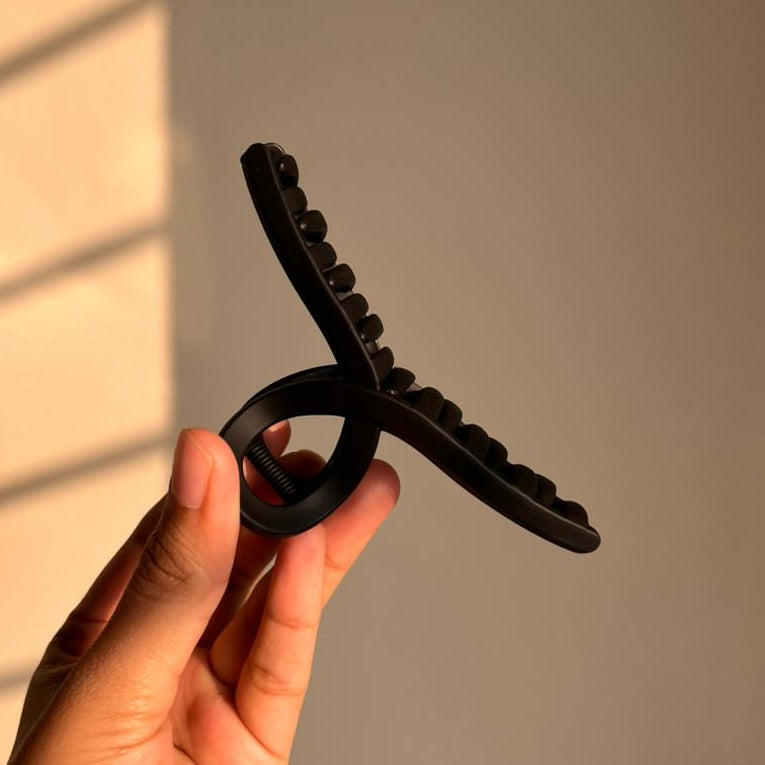 Hand holding a black hair clip against a neutral background