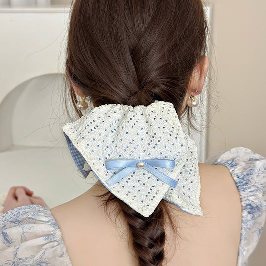 Woman with braided hair wearing a decorative hair accessory or a square shaped scrunchie with a blue ribbon.