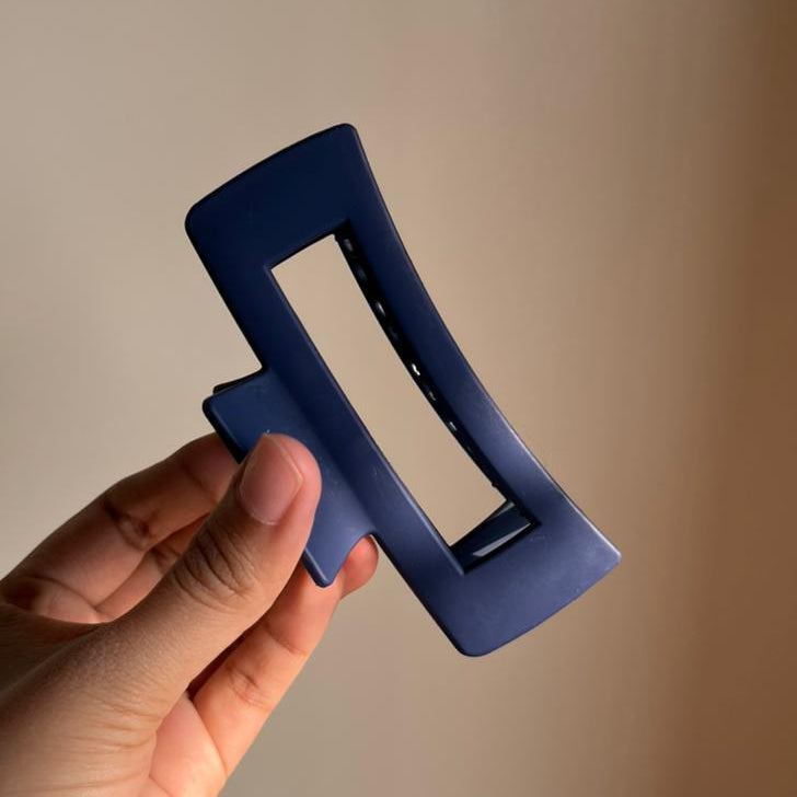 Hand holding a blue hair clip against a neutral background