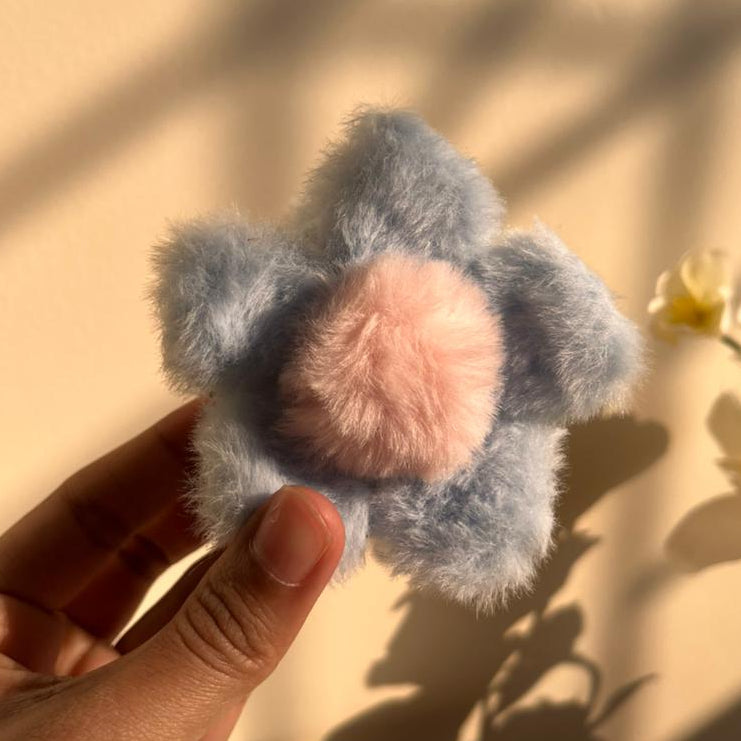 Fluffy blue and pink hair clip held by a hand against a beige background