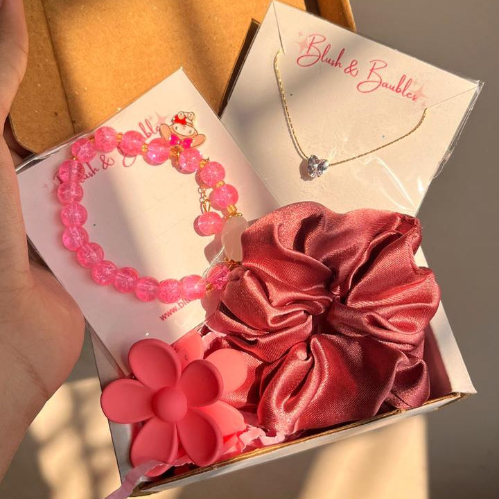 Pink hair accessories including a bracelet, scrunchies, and a necklace in an open box.