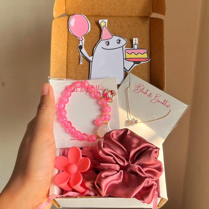 Gift box with pink hair accessories including a scrunchie, hair tie, and hair clip, held by a hand.