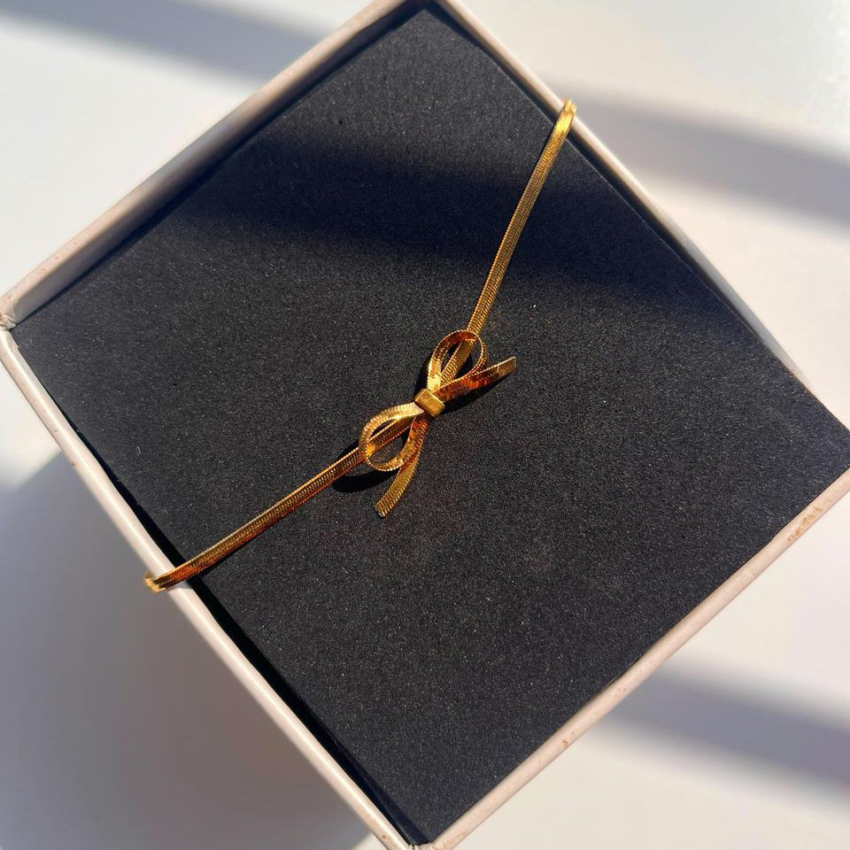 Gold bracelet tied in a bow on a black box with a white background