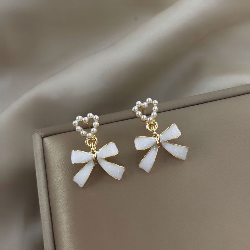 Bow-shaped earrings with pearl details on a beige fabric background