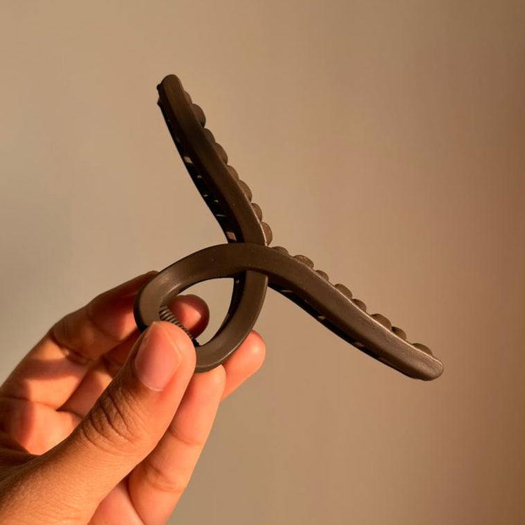 Hand holding a brown hair clip against a plain background