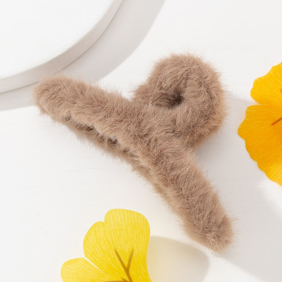 Fluffy brown hair clip on a white surface with yellow leaves