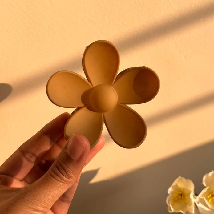 Hand holding a gold flower-shaped clip against a warm-toned background