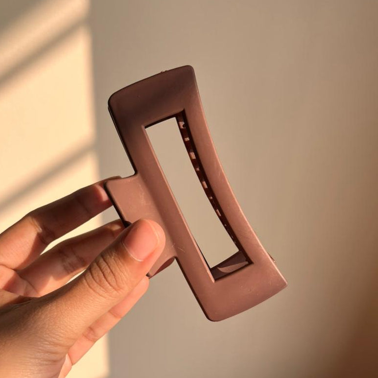 Hand holding a pink rectangular hair clip against a neutral background