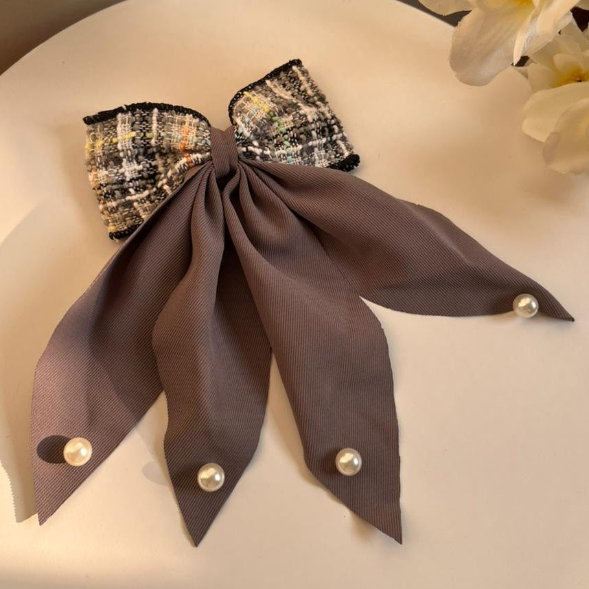 Decorative hair bow with pearl accents on a white surface with flowers in the background