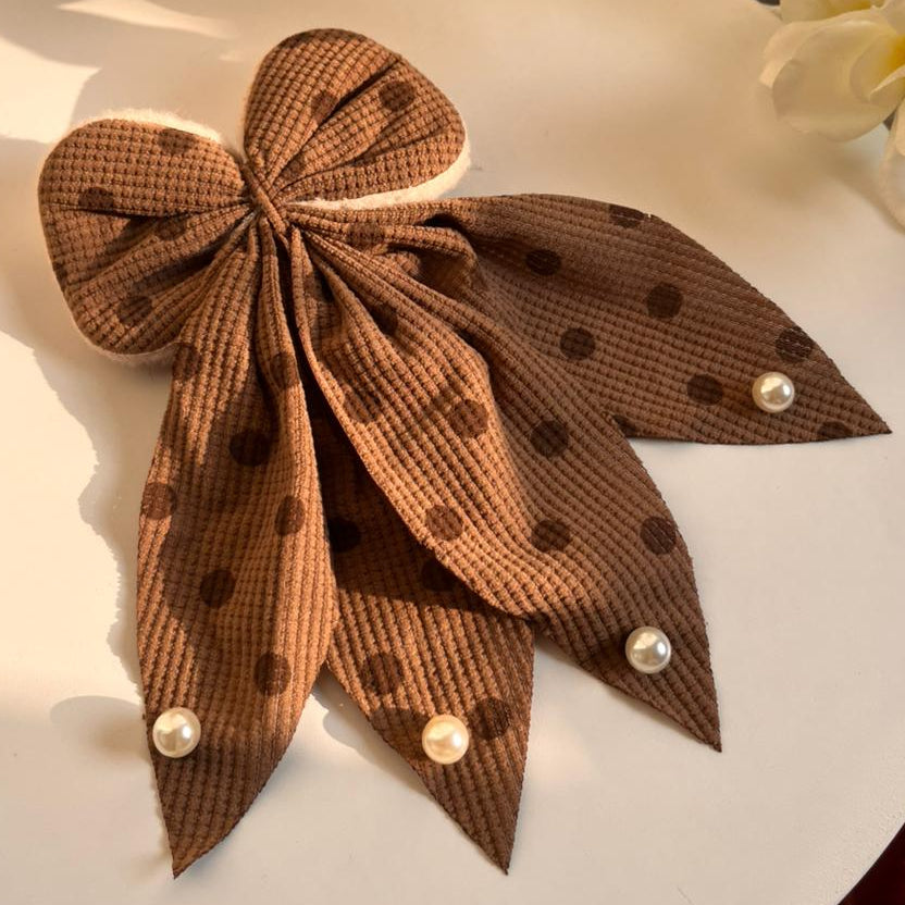 Brown polka dot bow with pearls on a white surface with flowers in the background
