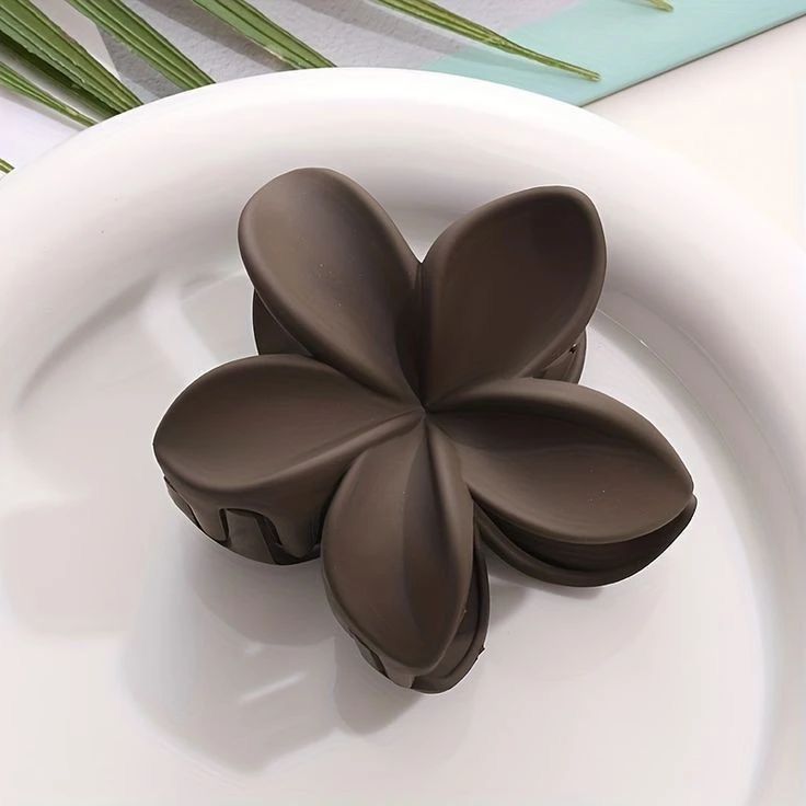 Brown flower-shaped hair clip on a white plate with green leaves in the background