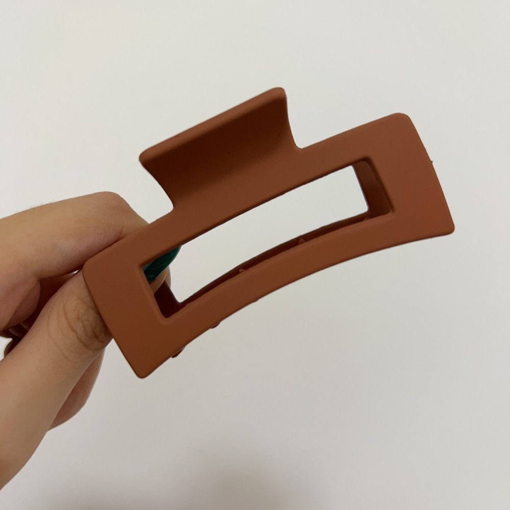 Hand holding a brown rectangular hair clip against a plain background