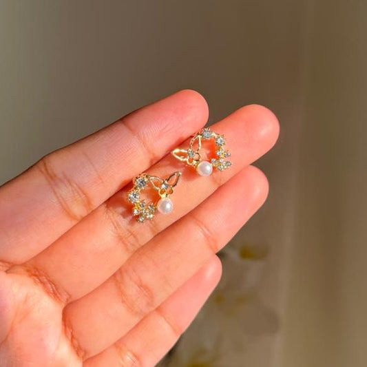 Hand holding a pair of decorative earrings against a neutral background