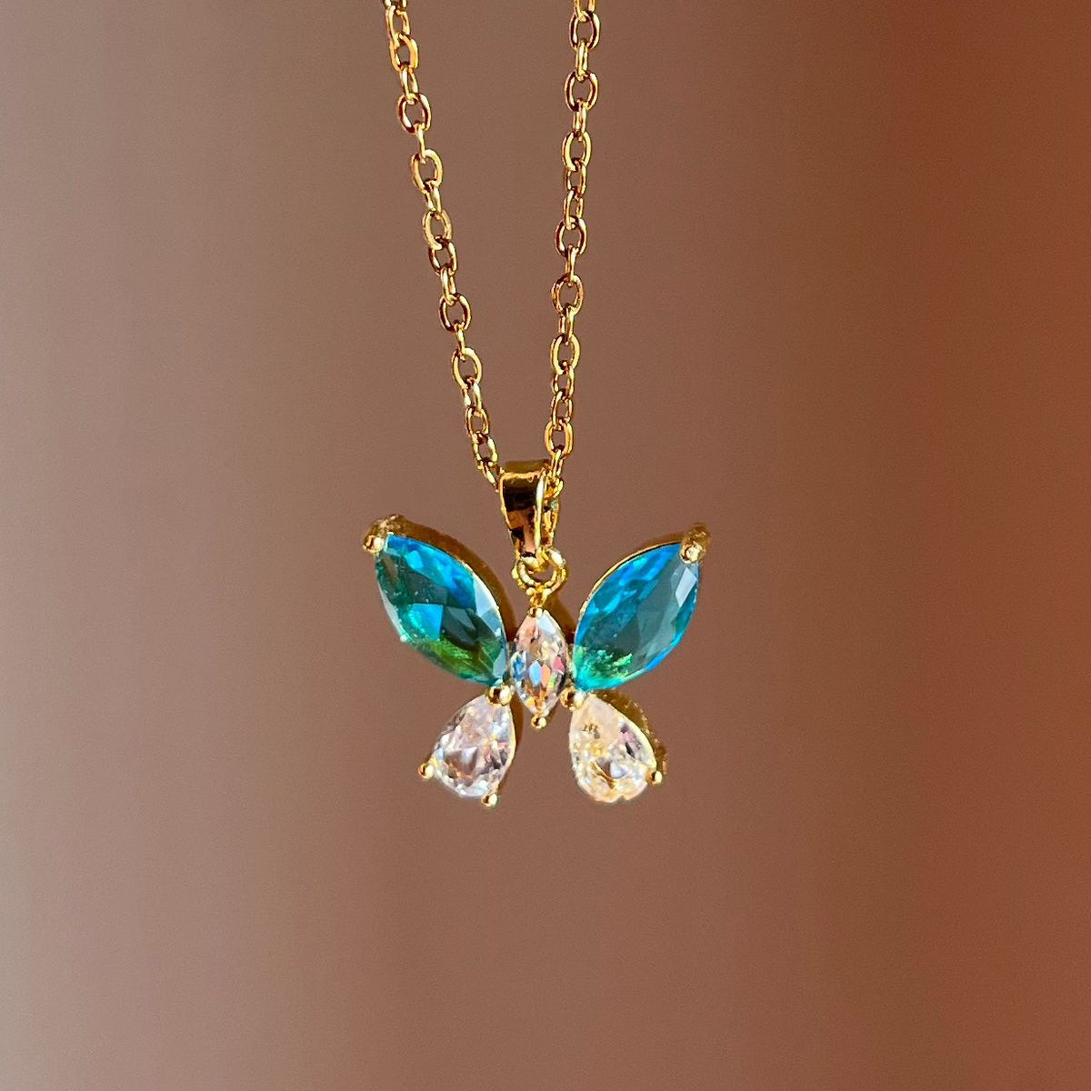 Butterfly-shaped pendant necklace with gemstones on a gold chain against a brown background