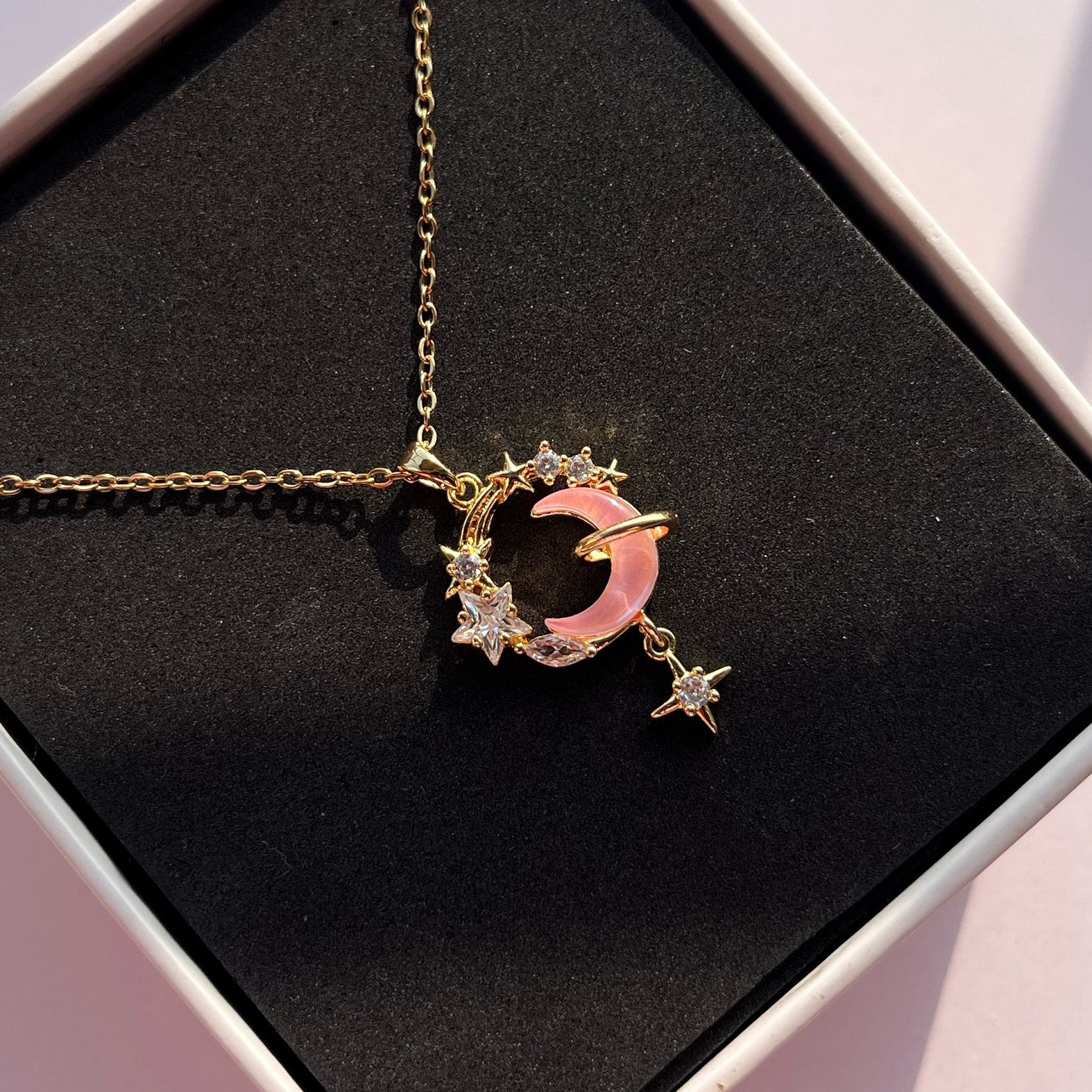 Necklace with a pink crescent moon and star pendant on a black background