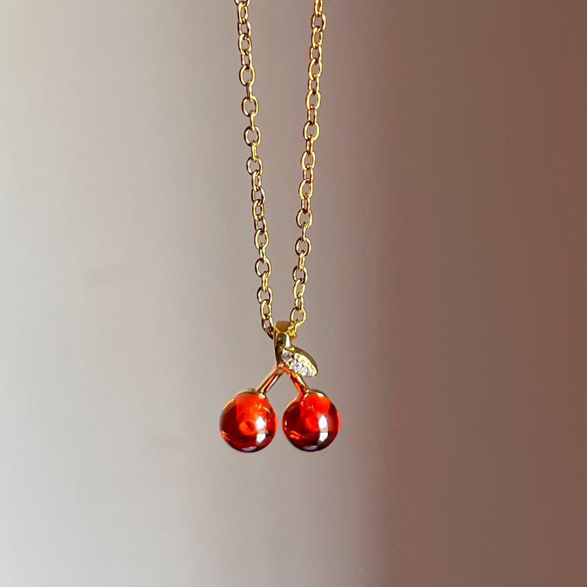Necklace with cherry-shaped pendants on a gold chain against a gradient background