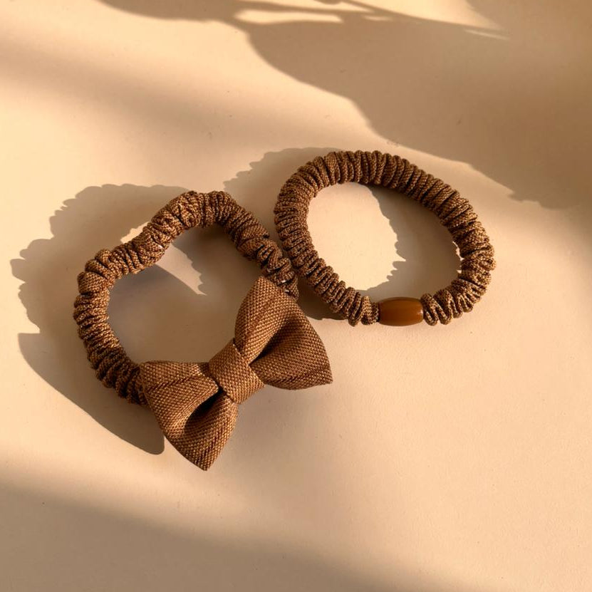 Two brown hair ties with a bow on a beige surface