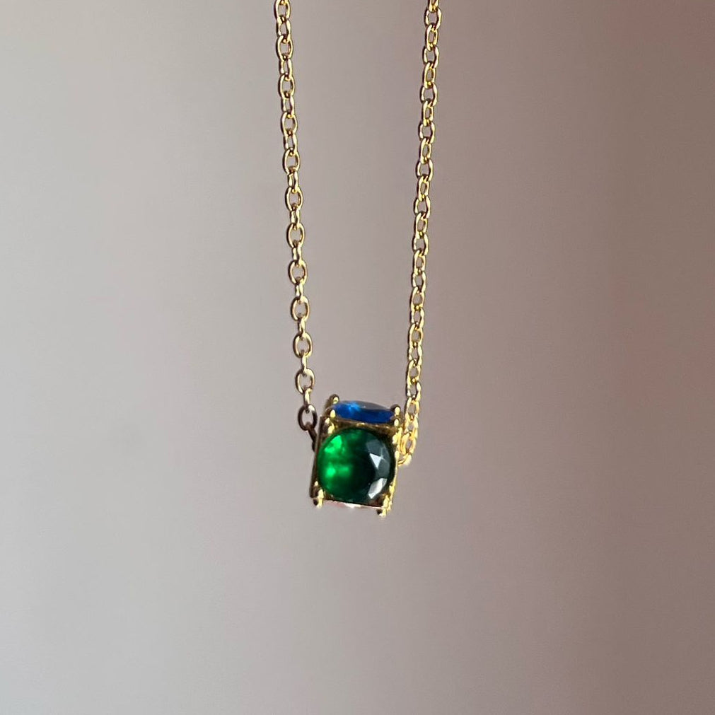 Gold necklace with a green gemstone pendant on a plain background