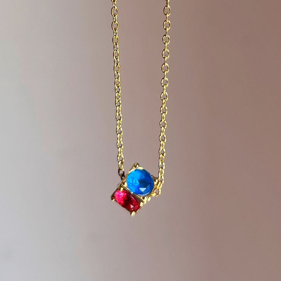 Gold necklace with blue and red beads on a plain background
