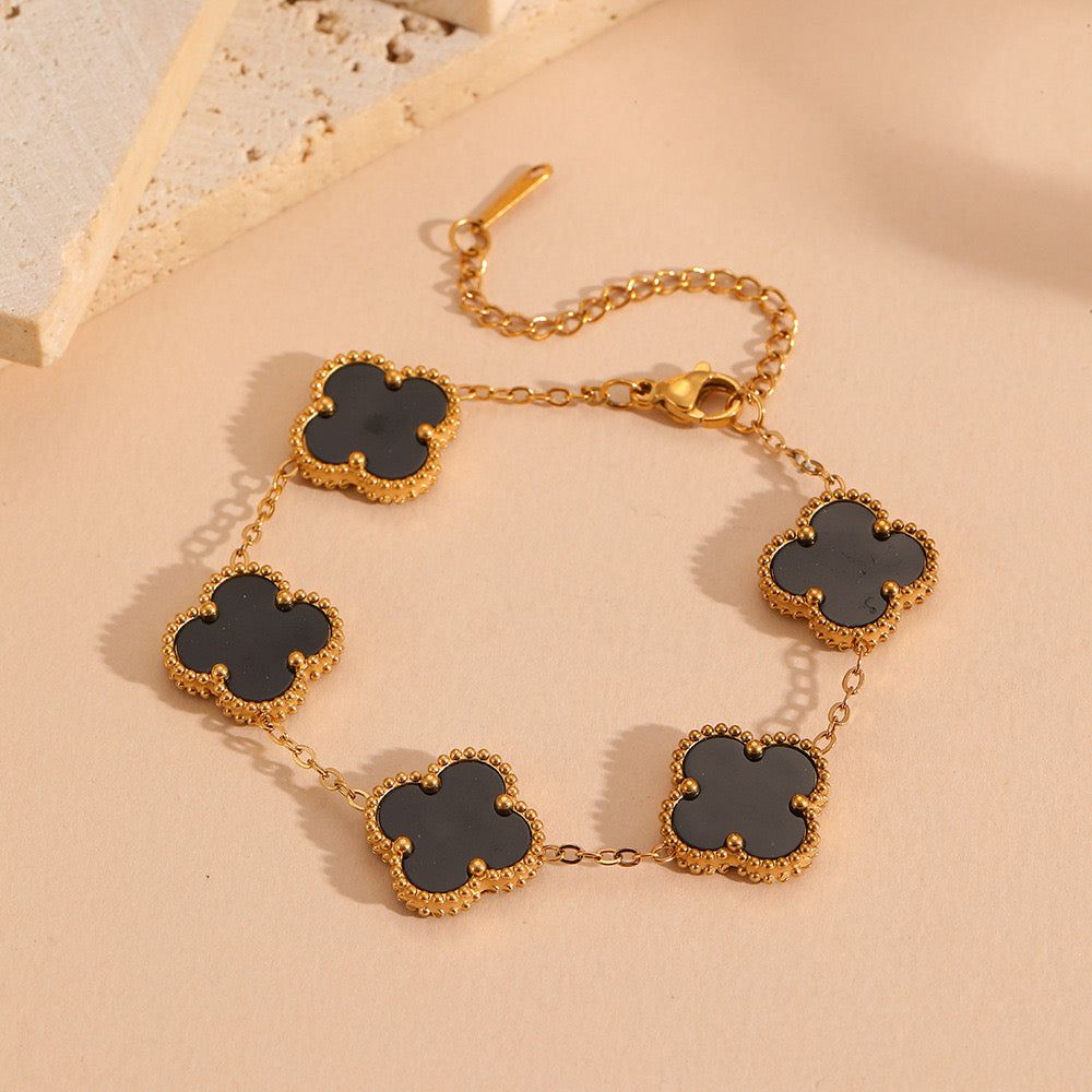 Gold necklace with black clover-shaped pendants on a beige background