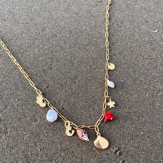 Gold necklace with various charms on a sandy surface