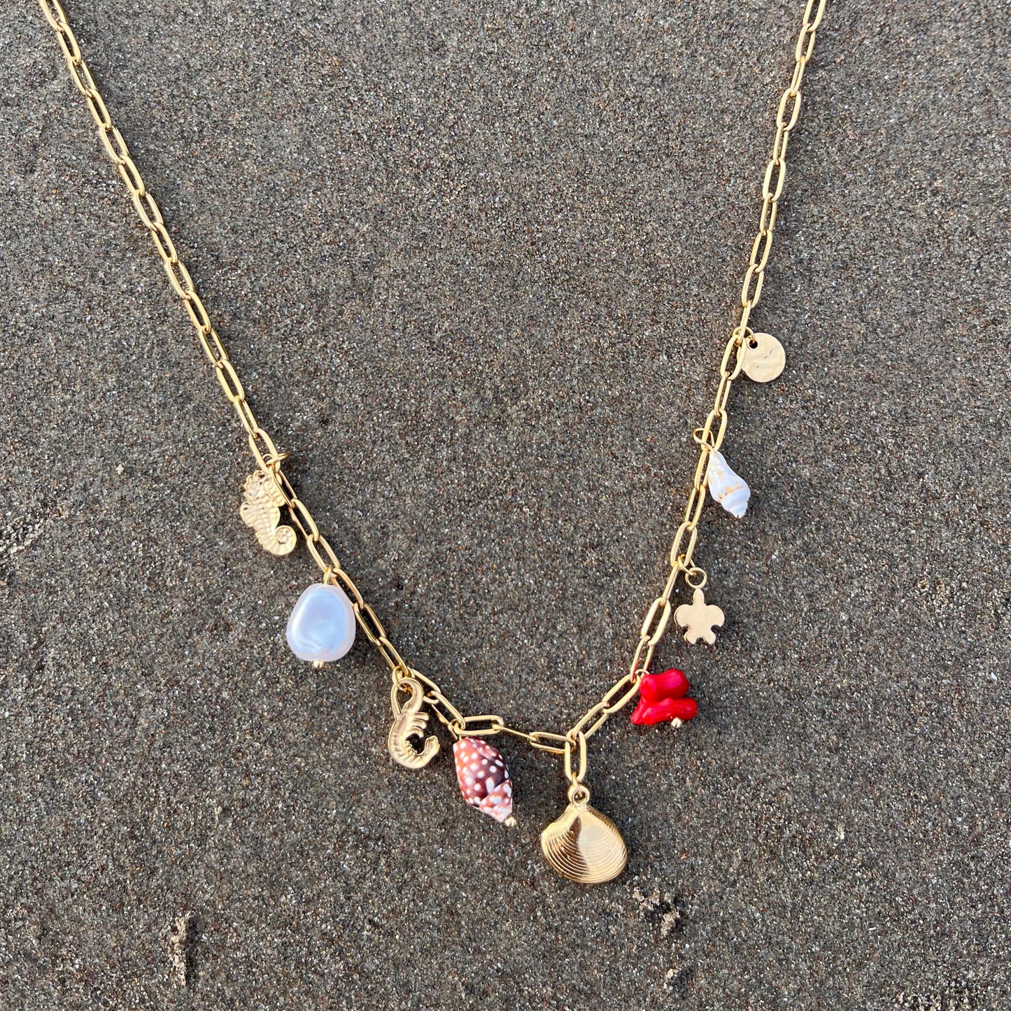 Gold necklace with colorful charms on a sandy surface