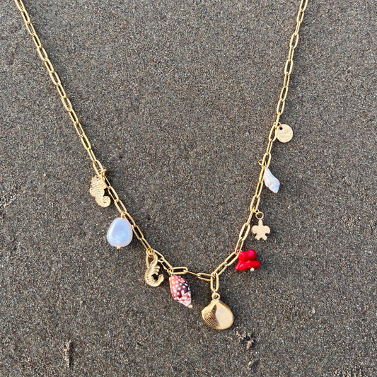 Gold necklace with colorful charms on a sandy surface