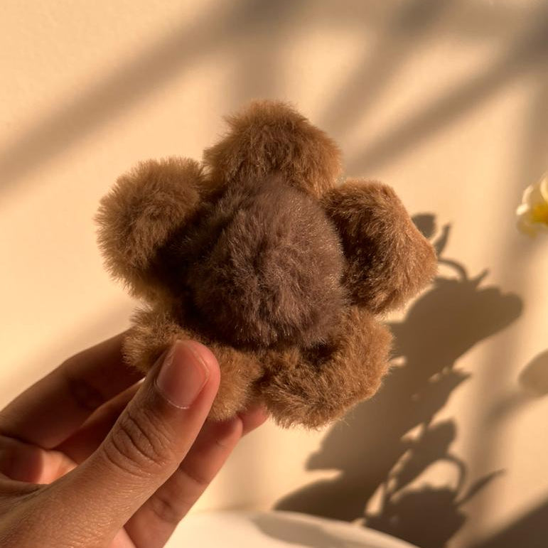 Brown fuzzy hair clip held in a hand with a soft light background