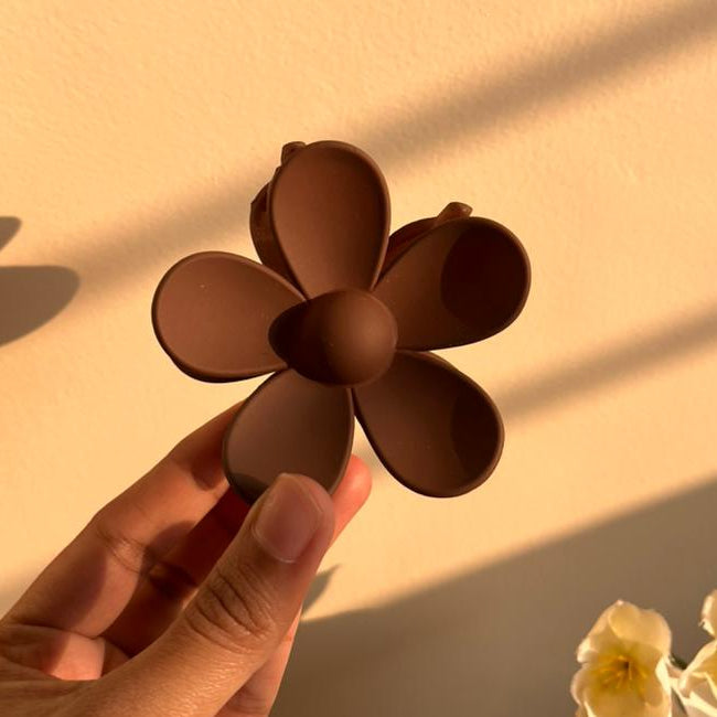Hand holding a brown flower-shaped clip against a beige background with shadows