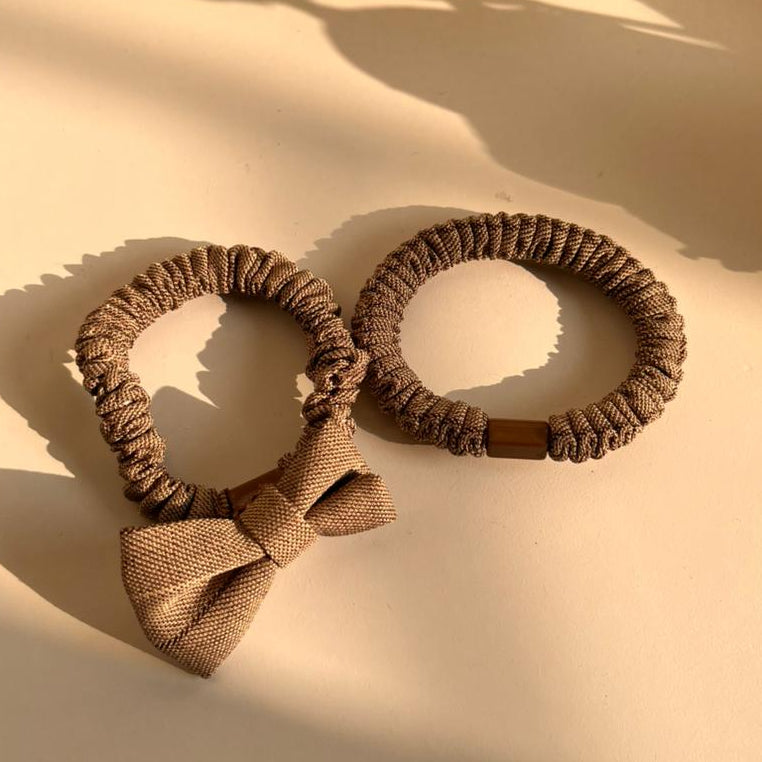 Two brown hair ties with a bow on a beige surface.