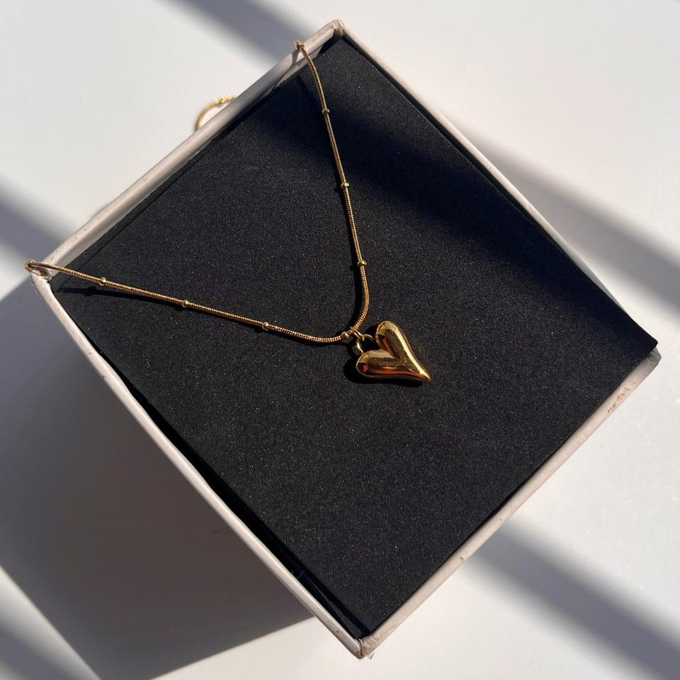 Gold heart-shaped necklace on a black box with soft shadows