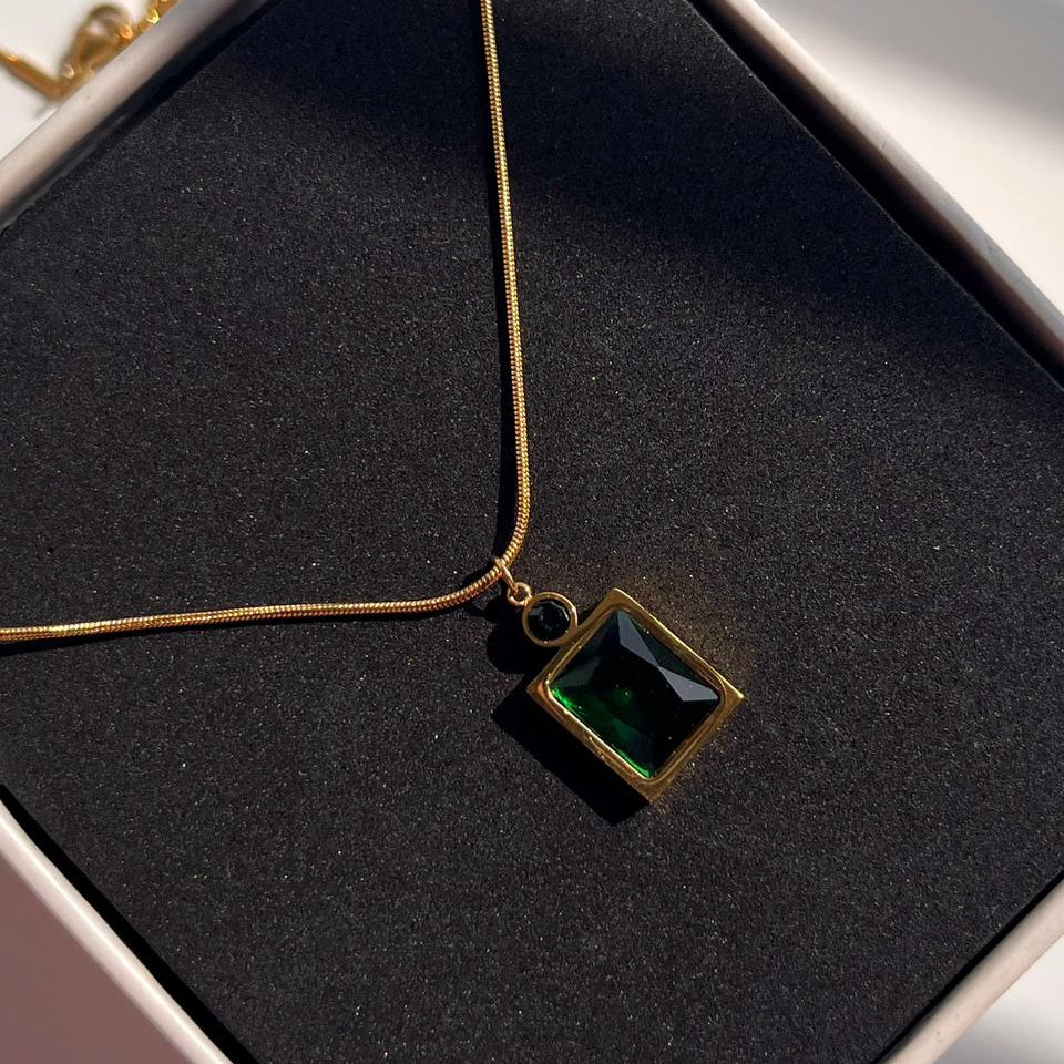 Gold necklace with a green pendant on a black cushion inside a jewelry box.