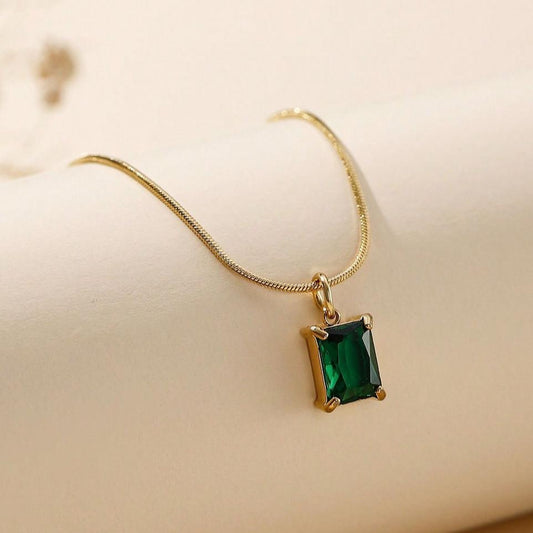 Gold necklace with a green gemstone pendant on a beige background
