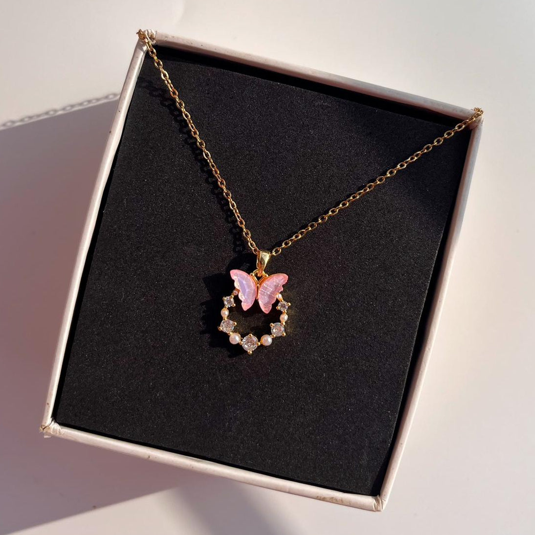 Necklace with a pink butterfly pendant in a black box on a light surface